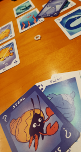 Picture of Q|cCards> game in progress. In the foreground, a hand of cards on a table, with more cards visible in the background.