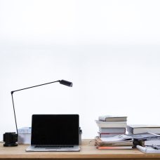 Työpöytä, jonka päällä on läppäri, lamppu ja kirjoja.