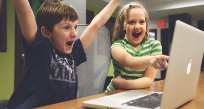 Kaksi lasta tietokoneen ääressä innostuneina.