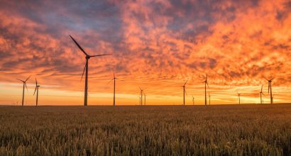 Modern windmills in a field, orange sky in the background.