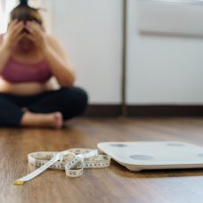 A photo of a person in sports wear sitting and holding their head, with measuring tape and scales on the floor.