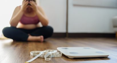 A photo of a person in sports wear sitting and holding their head, with measuring tape and scales on the floor.