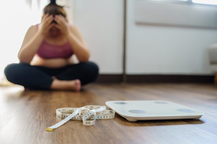 A photo of a person in sports wear sitting and holding their head, with measuring tape and scales on the floor.