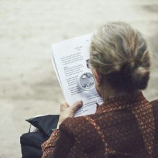 An older person reading a print with a magnifying glass.