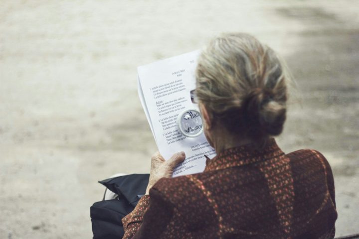 An older person reading a print with a magnifying glass.