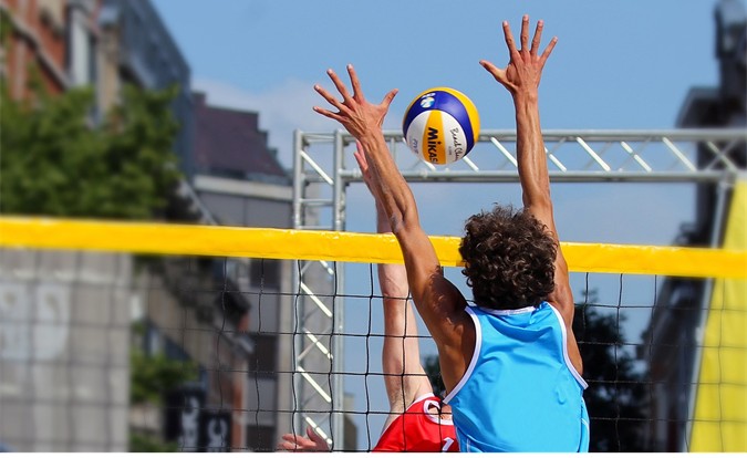 Lähikuva lentopallopelistä, jossa yksi pelaaja on lyömässä palloa verkon yli ja toinen puolustaa.