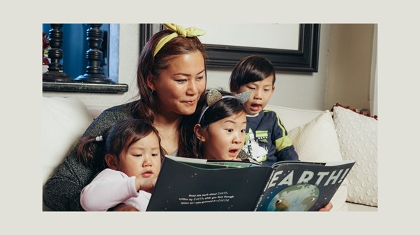 Aikuinen ja kolme lasta istuvat sohvalla ja katsovat kirjaa.