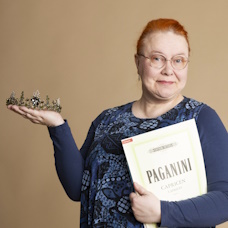 Sanna Qvick lähikuvassa, toisessa kädessään nuottivihko ja toisessa tiara.