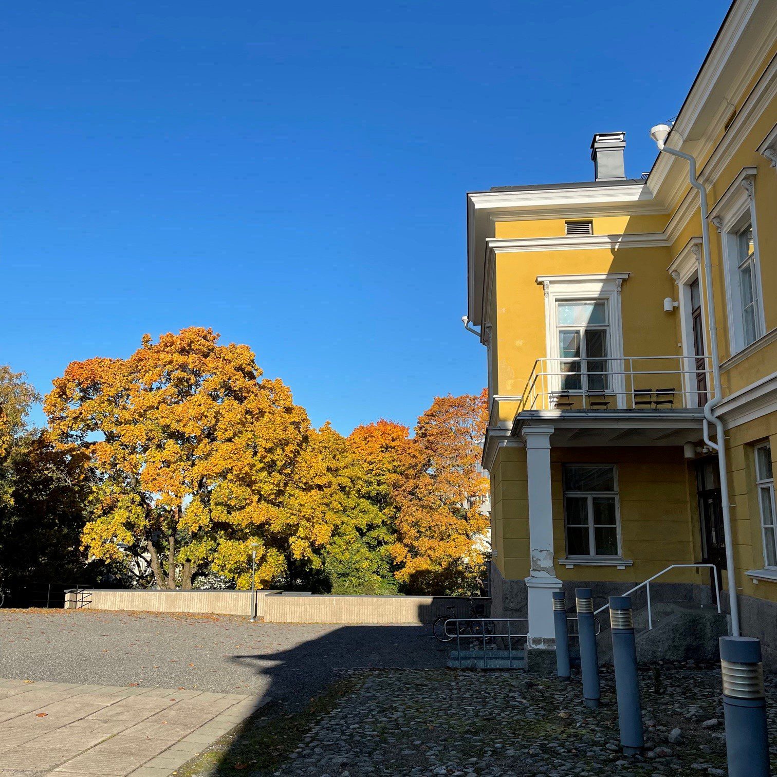 A yellow two-storey building with autumnal trees in the background