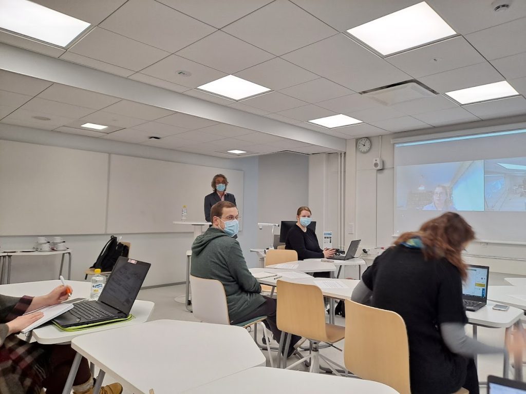 The image shows participants of the data workshop in a classroom, with two participants on the screen.