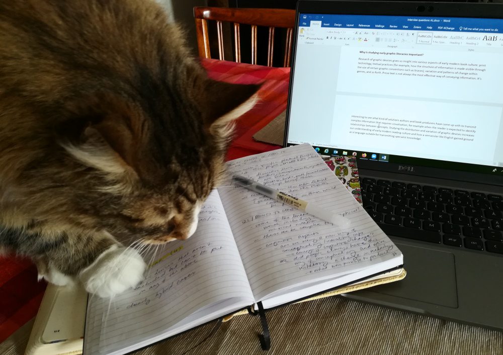 A cat on the desk inspecting an open notebook.