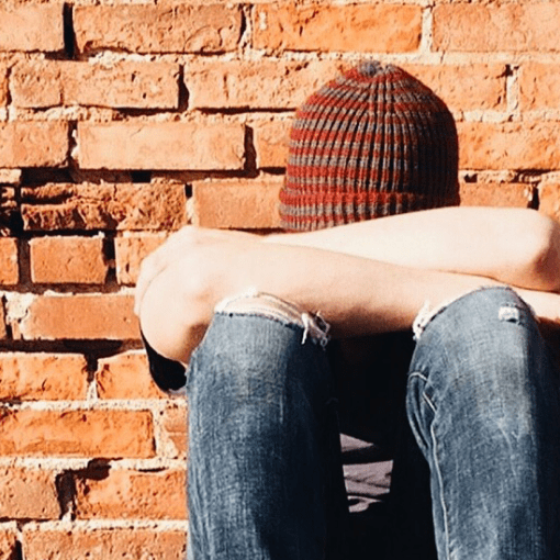 A person sitting head bend down in the front of the brick wall.
