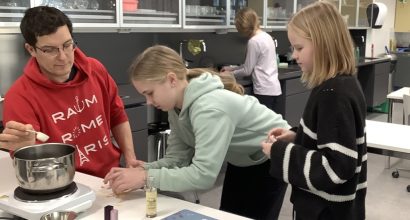 Miesopettaja auttaa kahta oppilasta purkittamaan itsetehtyä hunajaa koululuokassa.