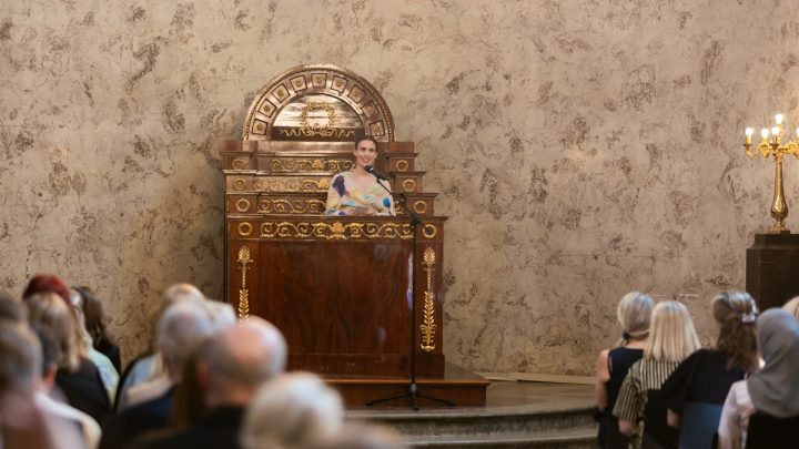 Nainen pitää juhlapuhetta isossa salissa.