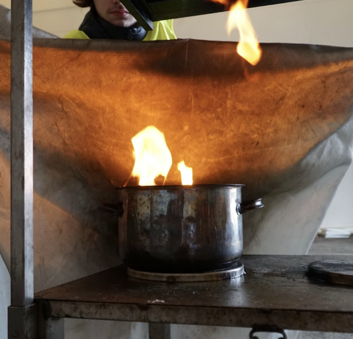 Pelastaja sammuttaa sammutuspeitolla liekehtivää kattilaa.