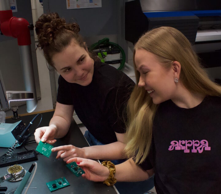 Kaksi ihmistä tekevät juottotyötä pöydän ääressä.