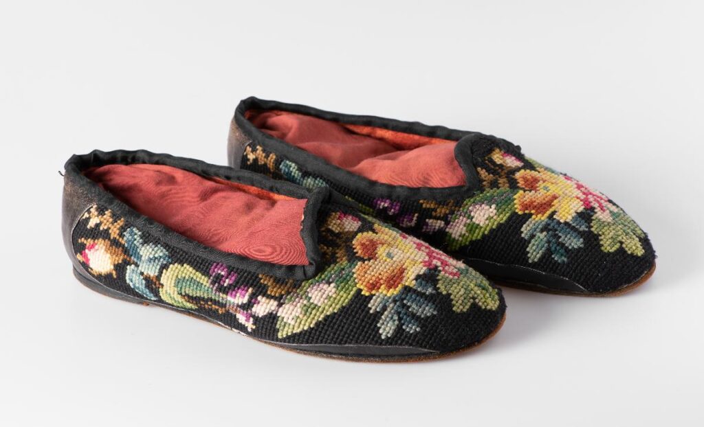 Mustat tohvelit, joihin on kirjailtu erivärisiä kukkia. Sisäkangas punainen.