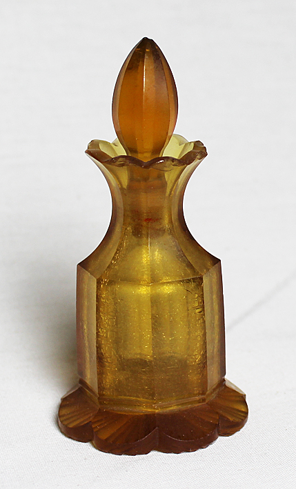 Rusehtavan värinen hajuvesipullo, jonka suu ja alusta näyttävät kukan terälehdiltä.