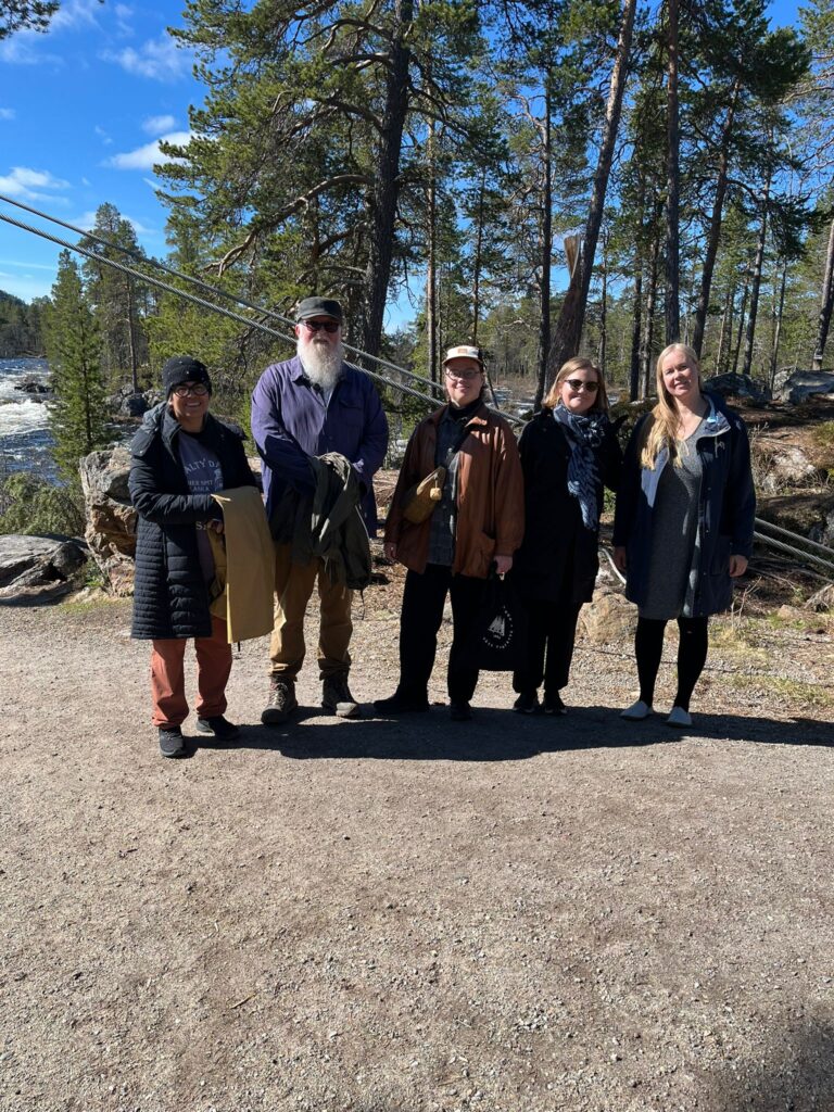 Kuvassa viisi henkilöä joen rannalla.