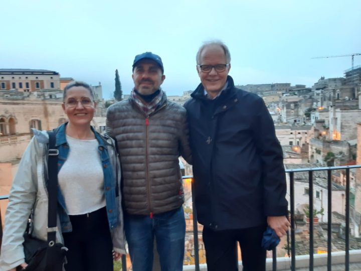 Kolme hymyilevää ihmistä vierekkäin italialaisella parvekkeella.
