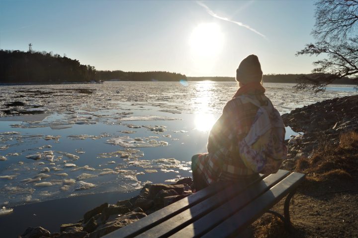 Turun yliopiston opiskelija istuu Ruissalossa penkillä, ja katselee mereltä nousevaa aurinkoa.