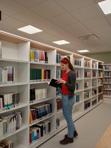 Kuvassa opiskelija selaa kirjaa Arcanumin kirjaston kirjahyllyn edessä.
