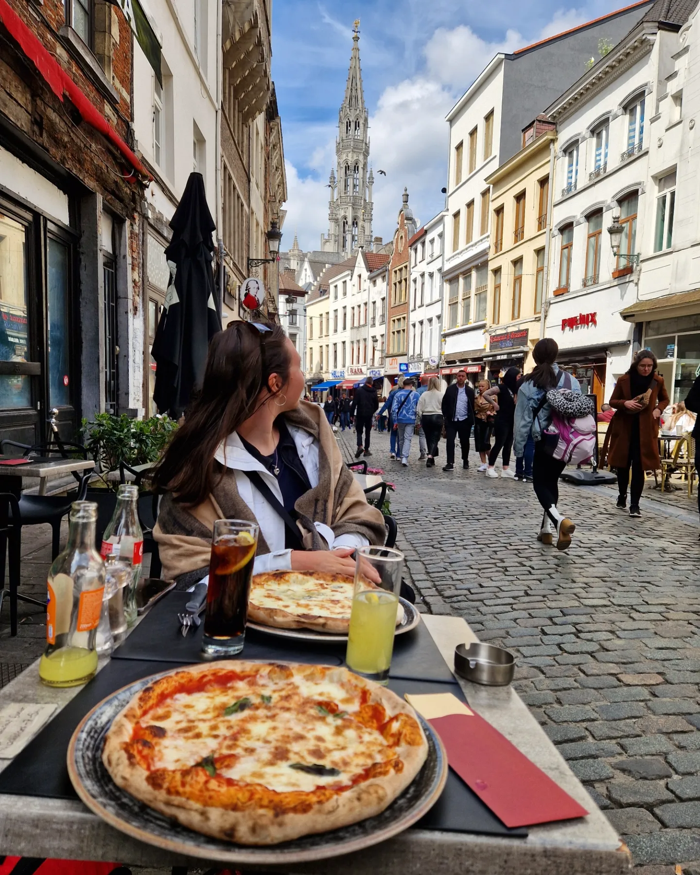 Opiskelijalähettiläs Petra ravintolan terassilla Brysselissä, taustalla kävelykatu ja katedraalin torni. 