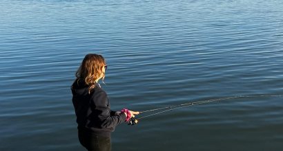 Kuvassa nainen kalastaa meren ääressä rantakalliolla