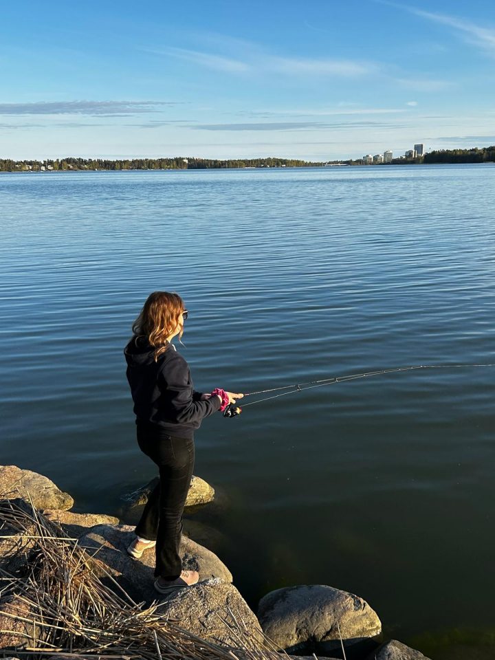 Kuvassa nainen kalastaa meren ääressä rantakalliolla