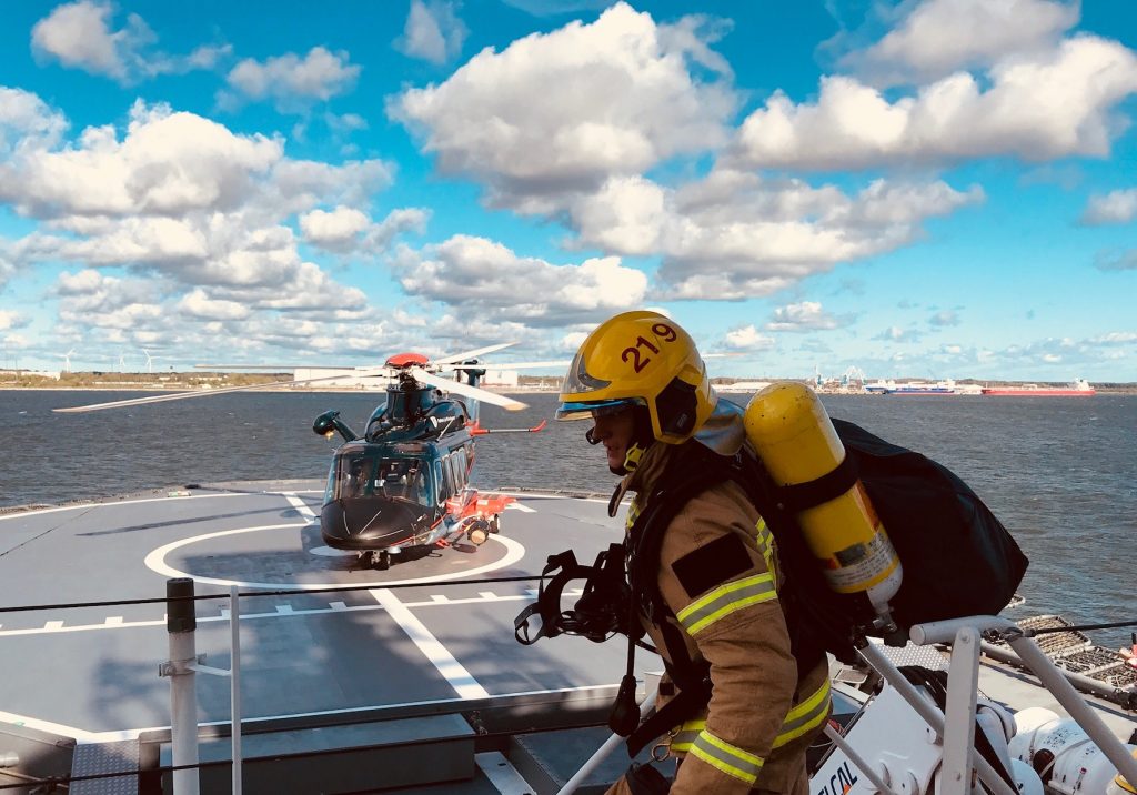 A rescue helicopter on the landing site of a patrol vessel and a maritime incident rescue officer heading towards it
