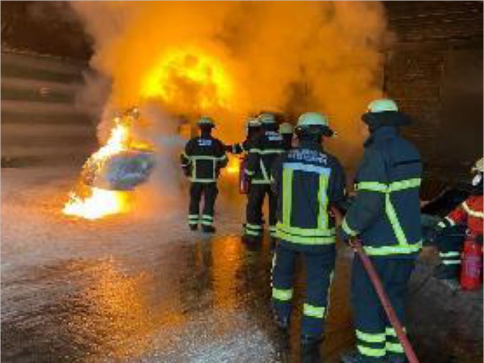 Four firemen dressed in their gear with yellow helmets on estinguishing a fire with a water hose inside a ship.