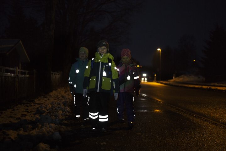 Schoolchildren wearing reflectors, walking along a road at night. 