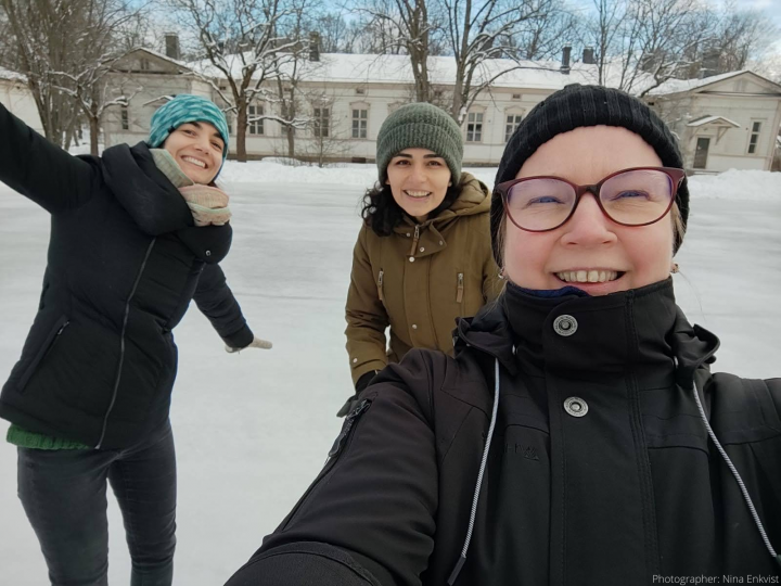 Three women in winter clothes standing on an outdoor ice rink.