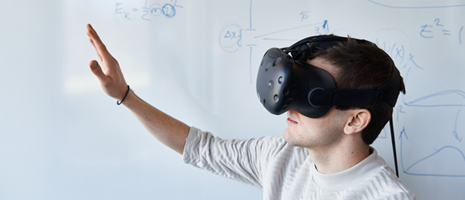 Image showing a student wearing a virtual reality headset and raising their right hand.