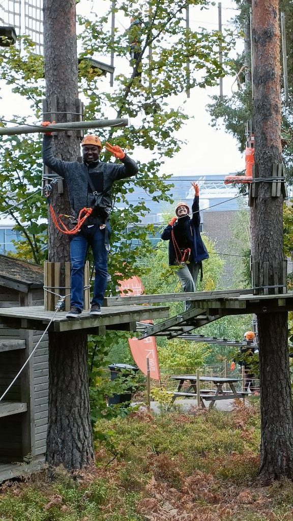 photo of excited man and woman giving the victory sign standing on planks in a zipline park in turku