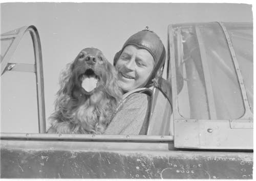 Lentäjäasuinen Karhunen istuu lentokoneessa ja pitelee sylissään läähättävää Peggy Brownia. 