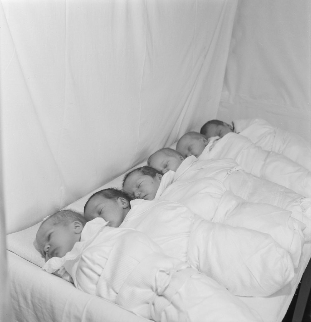 Kuusi vastasyntynyttä pienokaista nukkuu vieretysten sairaalan sängyssä.