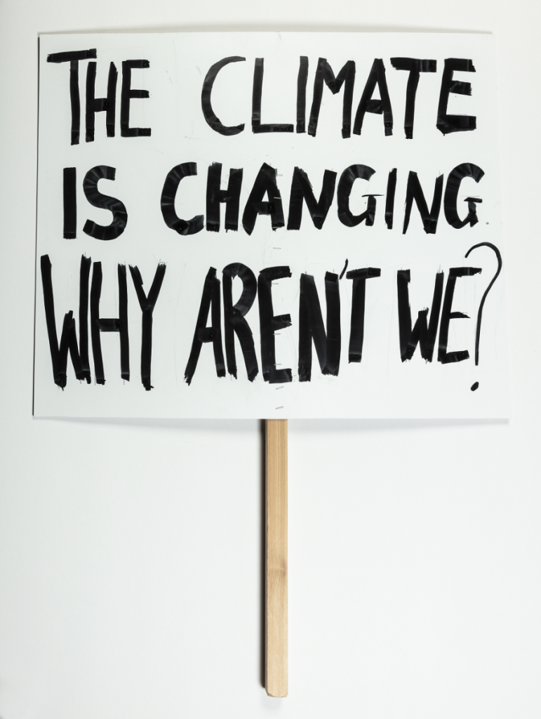 Valkoisessa kyltissä on mustalla tussilla kirjoitettu teksti: "The climate is changing, why aren't we?"