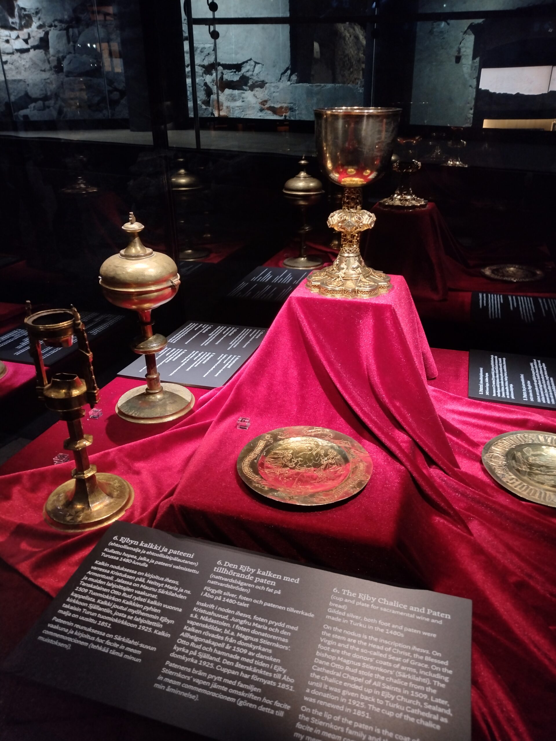 Museovitriinissä punaisen samettimaisen kankaan päällä olevia kullattuja koristeellisia astioita.
