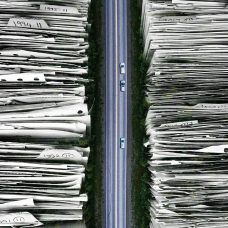 Tietokoneella tehty kuva, jossa kulkee keskellä vertikaalisesti autotie ja sen molemmin puolin on kaksi suurta paperipinoa.