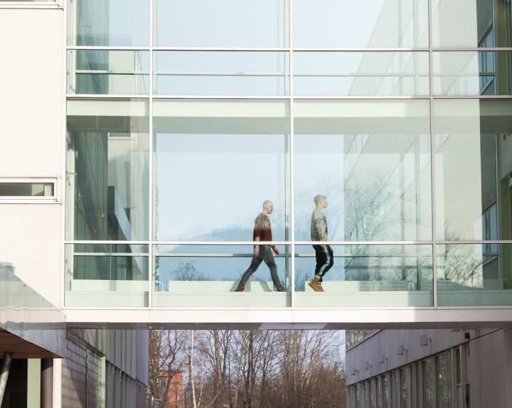 Kaksi ihmistä kävelee rakennusten välistä lasikäytävää.